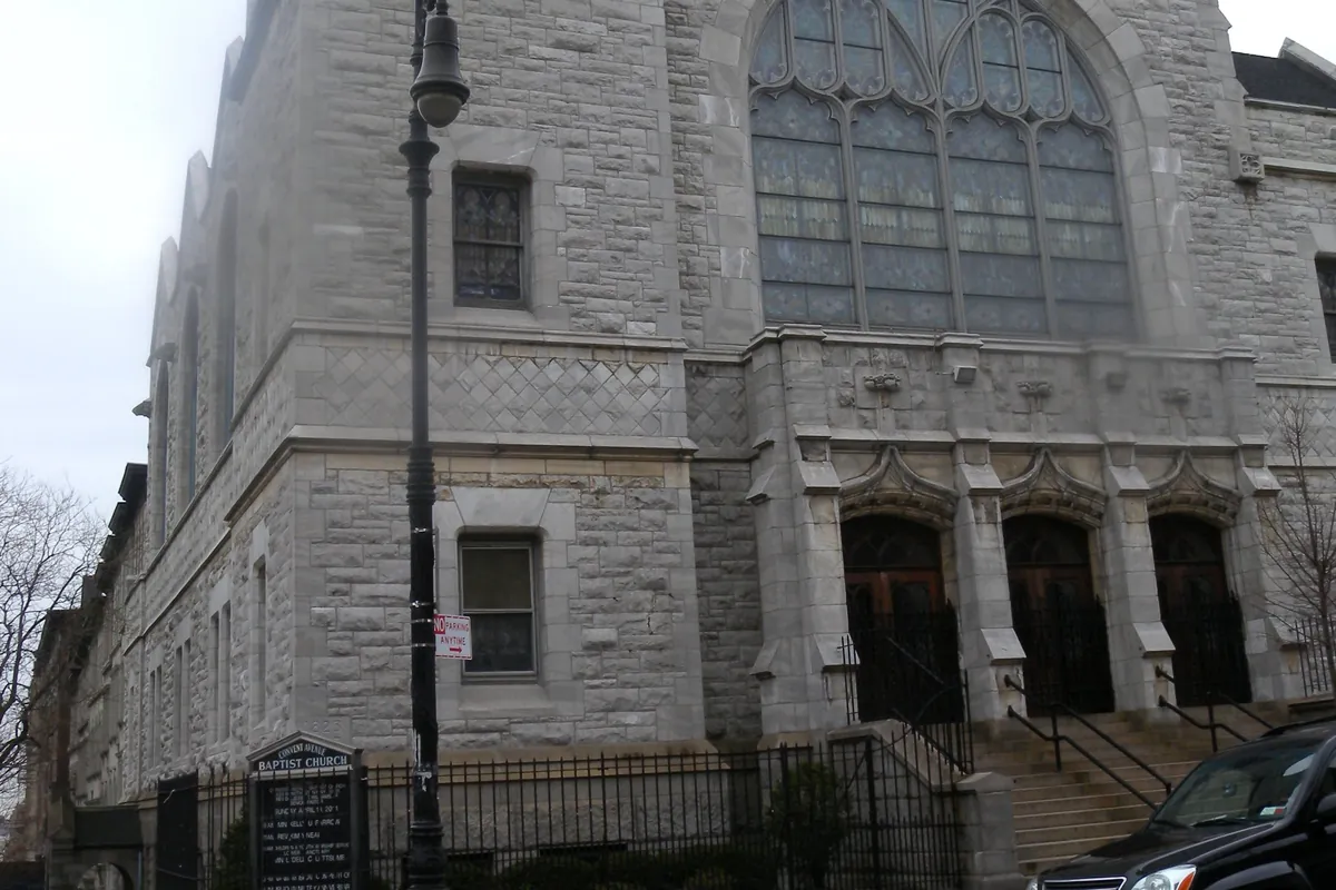La facciata gotica in pietra grigia di una chiesa di Harlem, con una torre quadrata, una grande vetrata ad arco e tre portali ad arco
